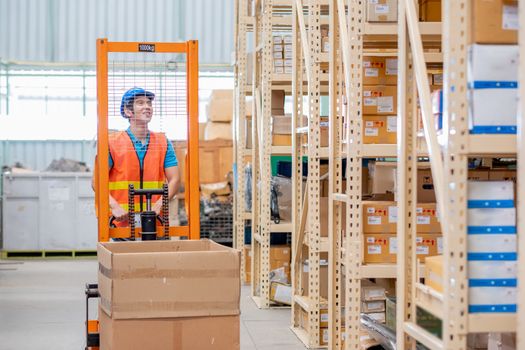 Warehouse Asian man or factory worker carry product with hand stacker or hydraulic cart in workplace area and look to shelves. Concept of good management system for delivery industrial business.