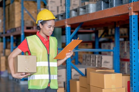 African American warehouse woman or factory worker check order or list of product and hold box in workplace area. Concept of good management of staff working in delivery industrial business.