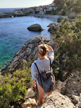 Young active feamle tourist wearing small backpack walking on coastal path among pine trees enjoing beautiful costal view of Velo Zarace beach on Hvar island, Croatia. Travel and adventure concept.