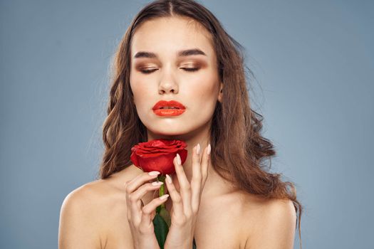 Woman portrait with red rose near the face on gray background and makeup curly hair. High quality photo