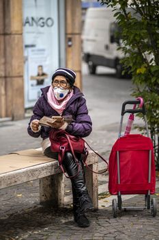 terni,itali november 05 2020:elderly oriental woman with medical mask sitting on a bench on the phone