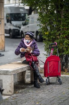 terni,itali november 05 2020:elderly oriental woman with medical mask sitting on a bench on the phone