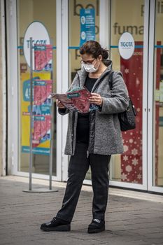 terni,itali november 05 2020:woman wearing medical mask in front of a shop looking at a brochure