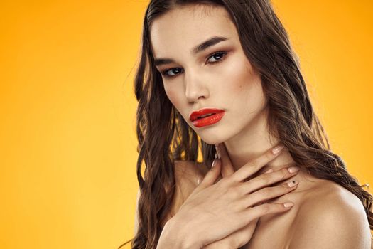 Beautiful brunette naked shoulders bright makeup red lips hairstyle close-up yellow background. High quality photo