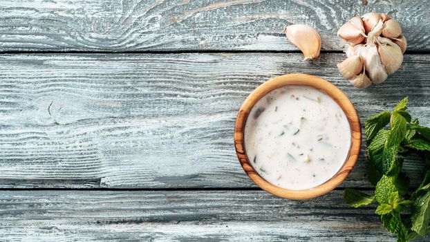 Authentic pakistani cucumber raita sauce on gray wooden background. Raita sauce dip with cucumber, onion and tomato add-ins in small metal bowl and glass jar. Top view or flat lay. Copy space. Banner