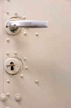 Old white metal door with lock, key and heck or door handle.