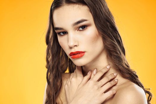 Beautiful brunette naked shoulders bright makeup red lips hairstyle close-up yellow background. High quality photo