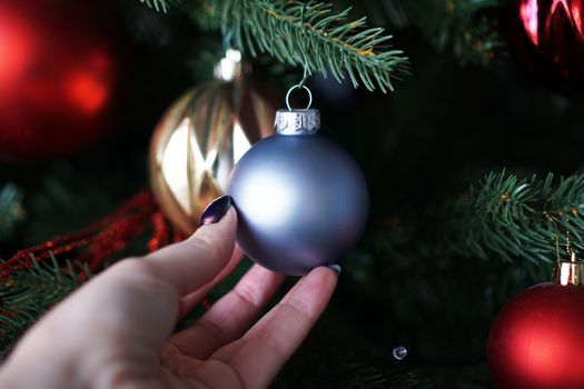 Female hand holds a blue Christmas ball on the background of a Christmas tree