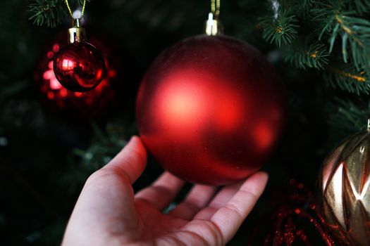 Female hand holds a red Christmas ball on the background of a Christmas tree