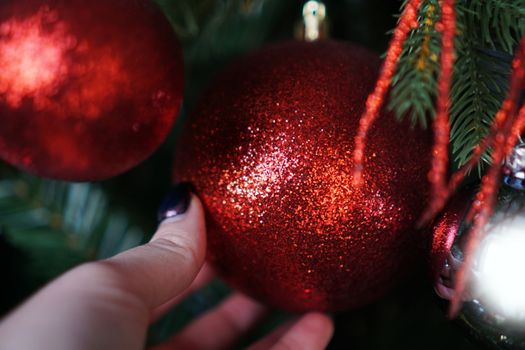 Female hand holds a red Christmas ball on the background of a Christmas tree