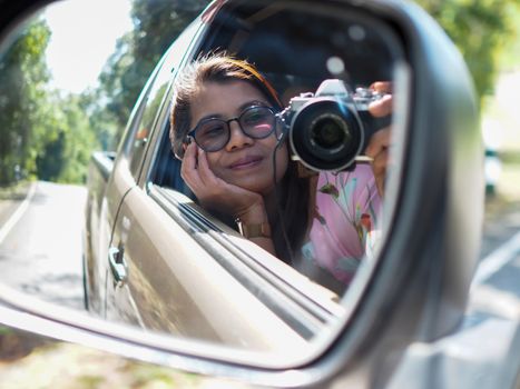 A young woman held a digital camera and took a picture of herself smiling reflected in the car mirror.
