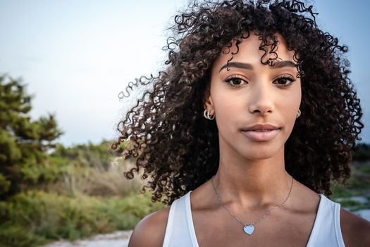 Femininity and beauty in nature: close up portrait of beautiful black Hispanic young woman with curly dark long hair looking confident at the camera - Make-up female artist with perfect mouth and eyes