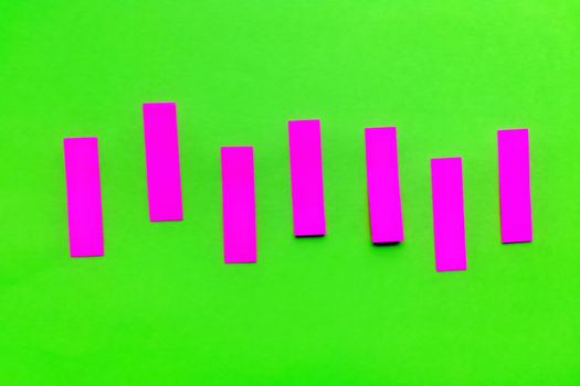 Purple pink vertical paper stickers on bright green paper. Horizontal shot. Front view.