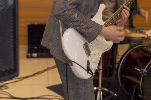 Grey suit and white guitar. There's a drum kit in the background.