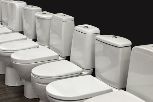 A row of white toilets. View from the side against a dark background. Market.