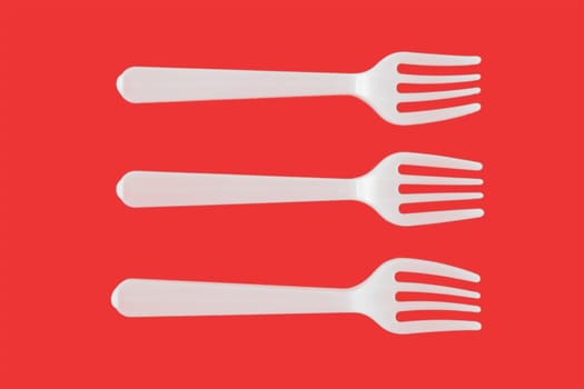 three plastic white forks on a red background
