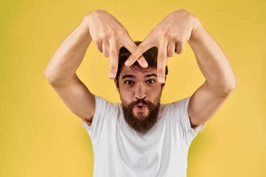 Bearded man emotions fun gesture with hands white t-shirt close-up yellow background. High quality photo