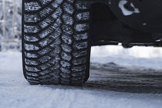 The wheel of the car is coated in winter tires in the snow.