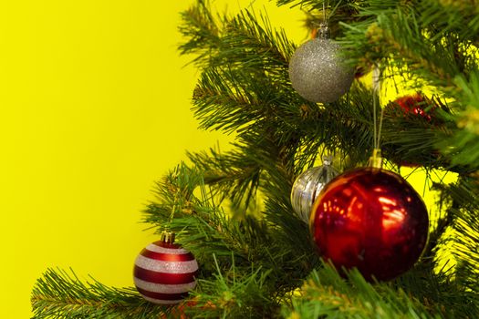 Part of the Christmas tree with balls of toys on a yellow background. View from the front. New Year.