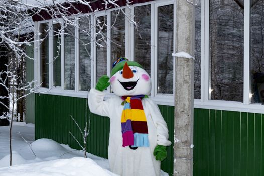 A snowman in a costume near a wooden building. Cristmas.