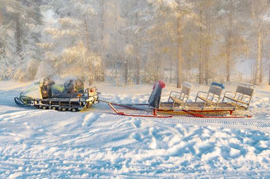 Snowmobile with sleigh in the winter forest. View from the side.