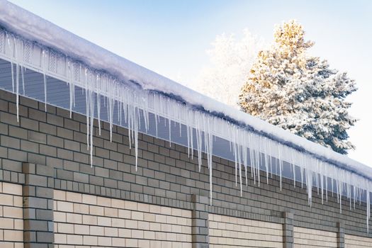 Ice icicles on the roof and the fence. The prospect is outgoing. Siberia.