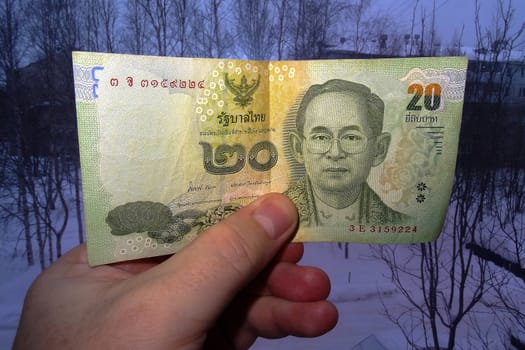 In the hand of 20 Thai baht against the backdrop of a dark city in Siberia. View from the front.