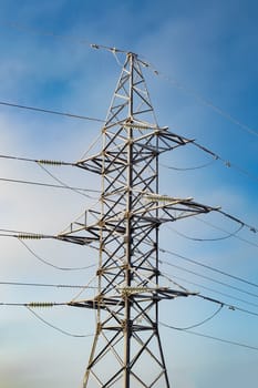 High-voltage electric line tower against a blue sky. View from side.