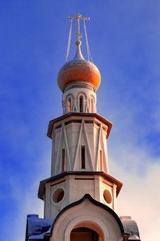 Bell tower of Orthodox Church in Russia against blue sky. View from front below.