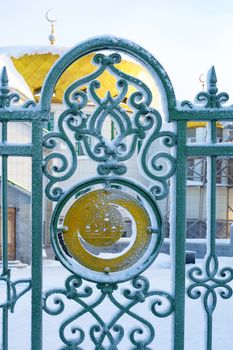 Metal green textured fence of mosque and building in winter in Siberia. View from the front.