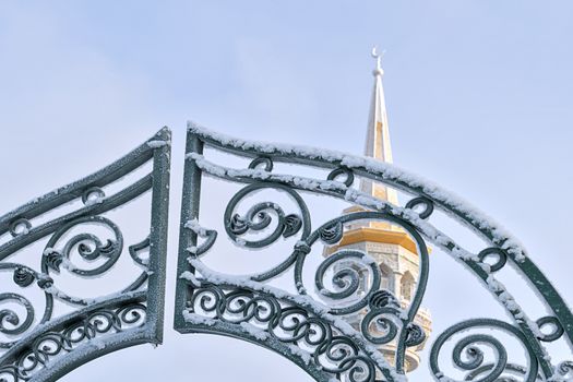 Gate to mosque and minaret in background against blue sky in winter. View from below.