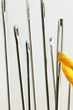 One  sewing needle with a yellow thread through the eyelet , several out of focus  needles in the foreground ,white background , studio shot , vertical composition ,macro photography