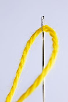 One  sewing needle with a yellow thread through the eyelet ,long tool with a hole at one end ,white background , studio shot , vertical composition ,macro photography 