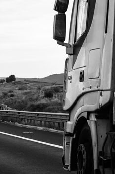 Black and white photo, concept of motion, loaded European truck in motion on asphalt road, transportation and delivery concept. Bucharest, Romania, 2020