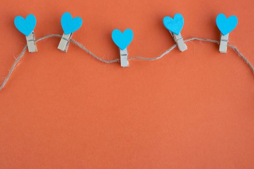 Small clothespins and blue hearts on a rope on an orange background