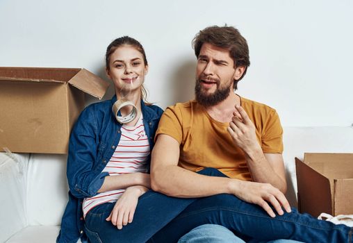 man and woman sitting on a white sofa in a room with boxes of things tools moving. High quality photo