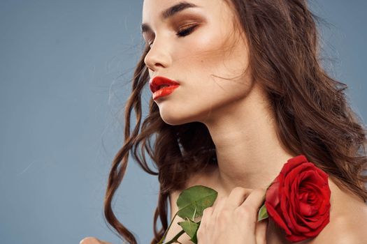 Woman portrait with red rose near the face on gray background and makeup curly hair. High quality photo