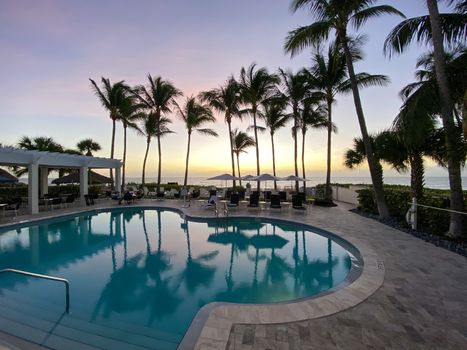 Naples, FL/USA - 10/30/20: Sunset overlooking the Gulf of Mexico with lounge chairs and palm trees at a tropical private beach club in Naples, Florida.