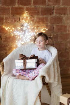 Merry Christmas, happy holidays. New Year 2021. little girl in pajamas opens a gift in living room on Christmas Eve.