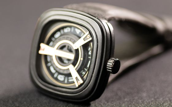 Square shaped used wrist watch on a slightly textured surface under studio lights macro photo