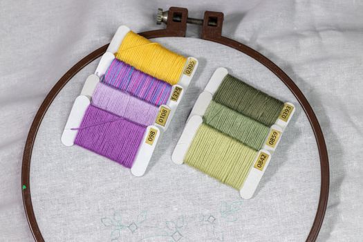 Wooden Embroidery hoop with a clean white piece of linen cloth and a simple design with a bunch of colorful threads on top.