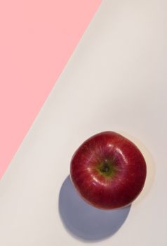 One bright red apple on a pink and white background ,beautiful colors ,studio shot ,top view,  vertical composition