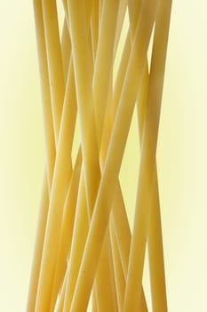 A group of Italian pasta called linguine on a  light background ,long flat yellow pasta , abstract effect ,vertical  composition