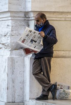 terni,italy november 06 2020:man leaning against a building reading the newspaper