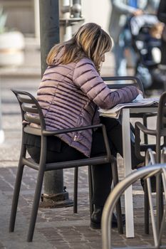 terni,italy november 06 2020:woman sitting at a table in a cafe reads the newspaper