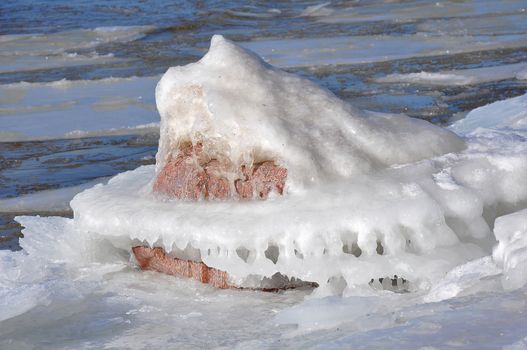 Sea shore in winter with ice frozen on a stone. Melting glacier in a global warming environment. Winter landscape. Icy beach and cold open water in the coast.