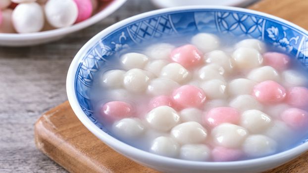 Close up of red and white tangyuan (tang yuan, glutinous rice dumpling balls) in blue bowl on wooden background for Winter solstice festival food.