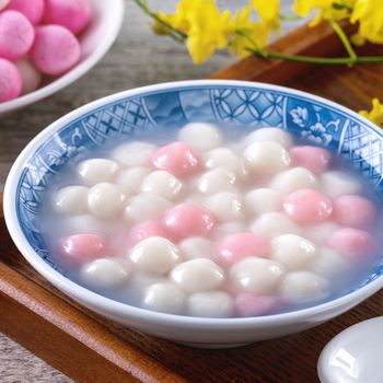 Close up of red and white tangyuan (tang yuan, glutinous rice dumpling balls) in blue bowl on wooden background for Winter solstice festival food.