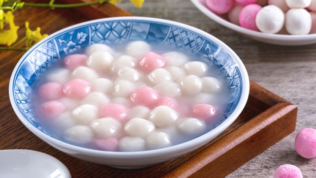 Close up of red and white tangyuan (tang yuan, glutinous rice dumpling balls) in blue bowl on wooden background for Winter solstice festival food.