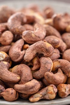 Cashew nuts with peel in a plate on wooden tray and table background, healthy raw food concept.